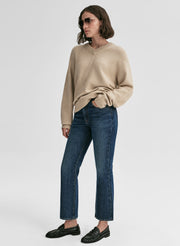 Person wearing a beige sweater and blue jeans on a white background