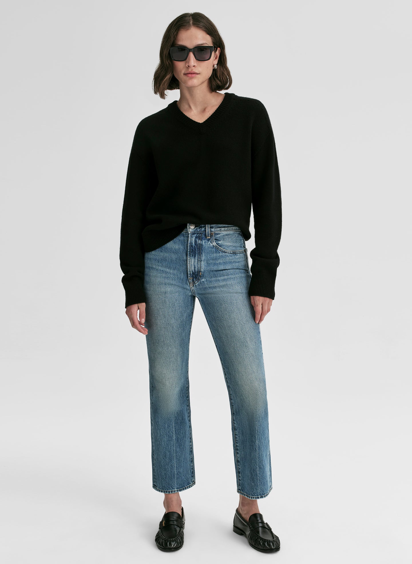 Person wearing a black sweater and light blue jeans on a white background