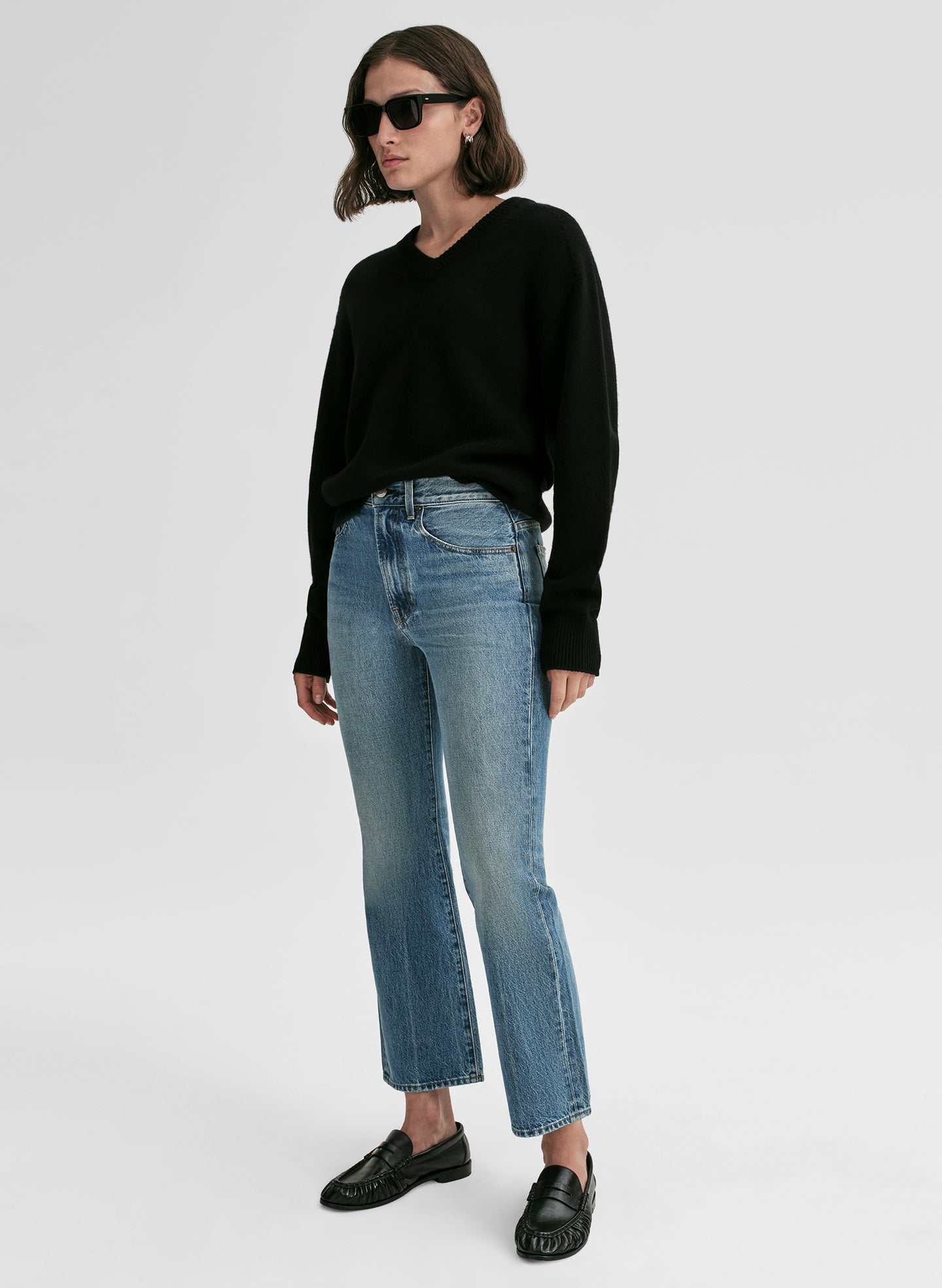 Person wearing a black sweater and blue jeans on a white background