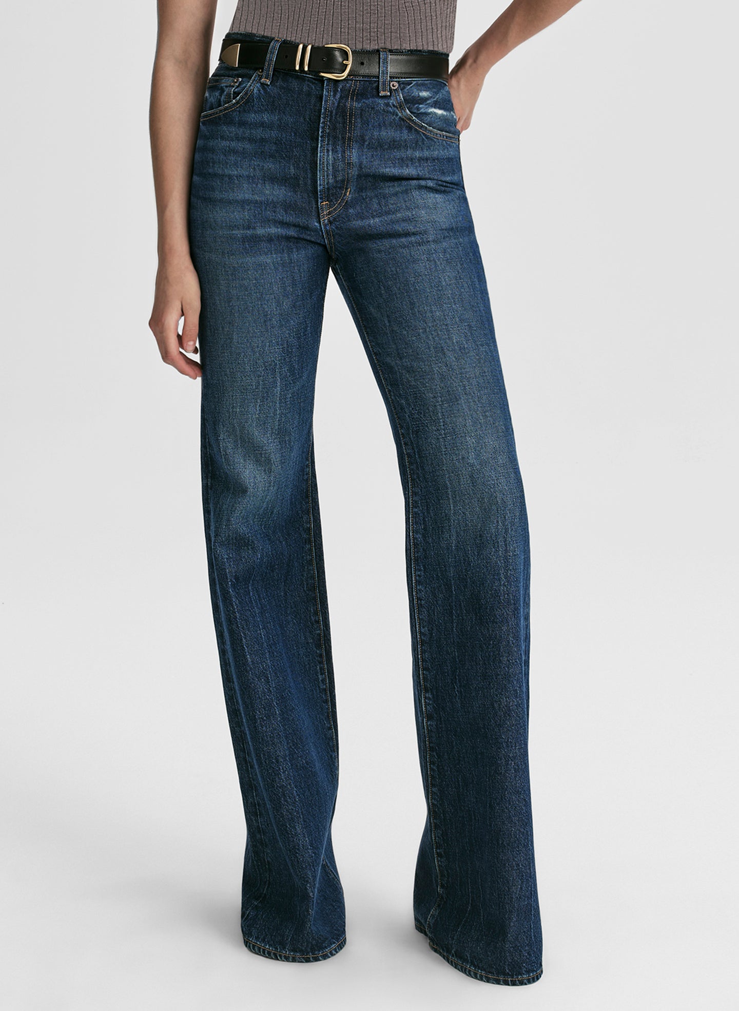 Woman wearing a grey sleeveless top and blue jeans on a white background