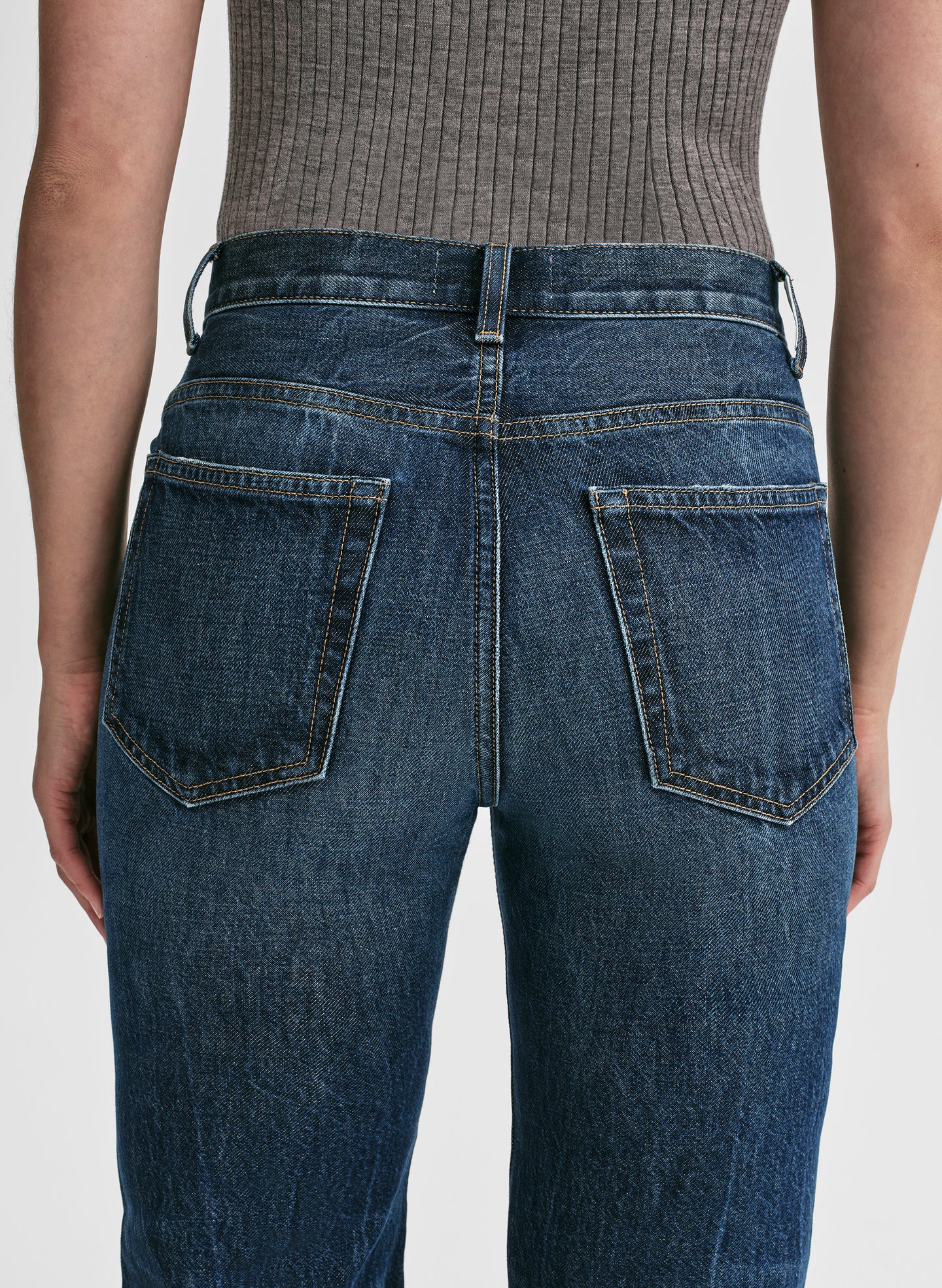 Woman wearing a grey sleeveless top and blue jeans on a white background