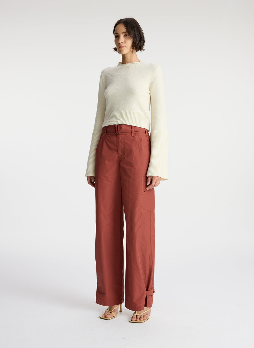 side view of a woman wearing a cream sweater and brown pants