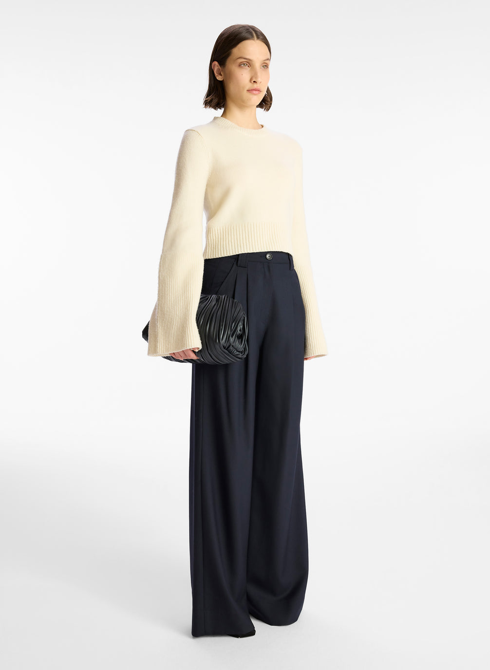 side  view of a woman wearing a cream sweater and navy wide leg pants