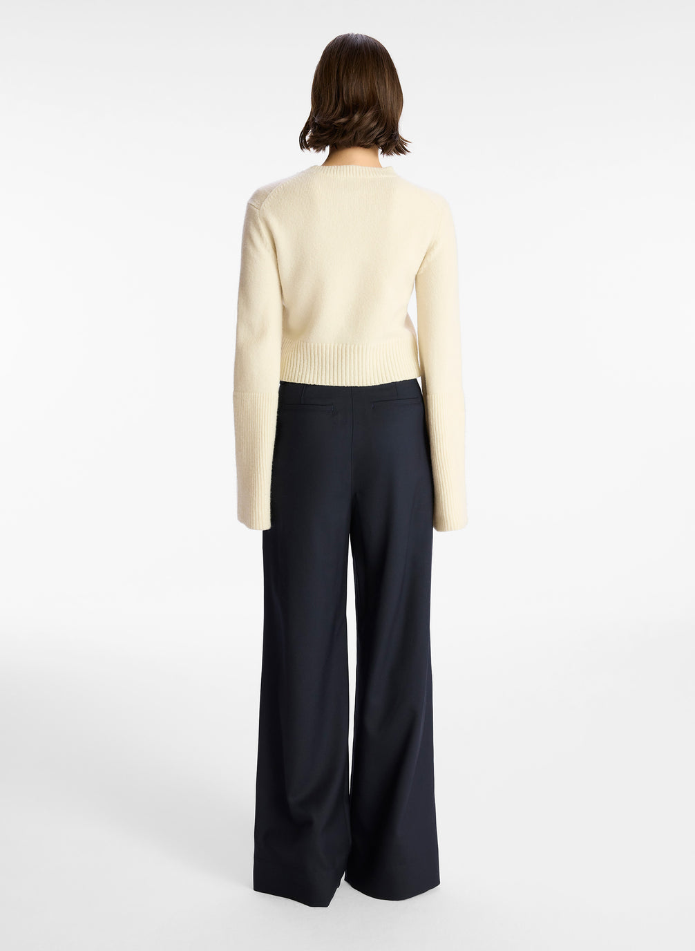 back  view of a woman wearing a cream sweater and navy wide leg pants
