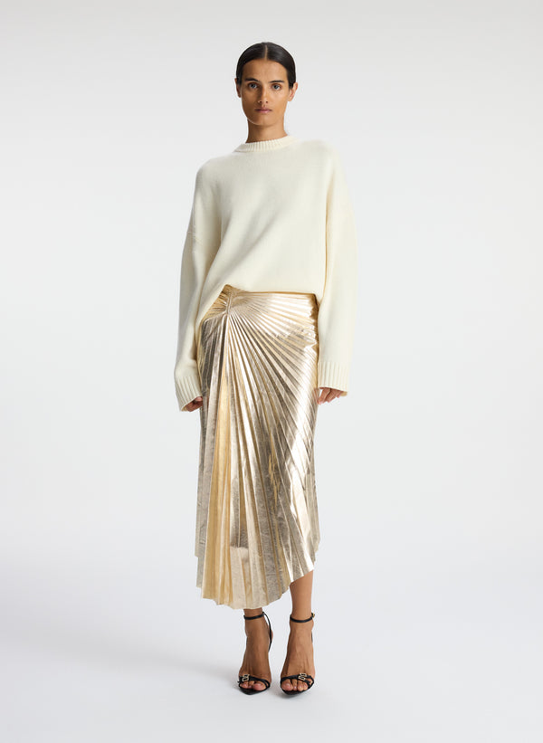 front view of woman wearing white sweated and metallic gold pleated midi skirt