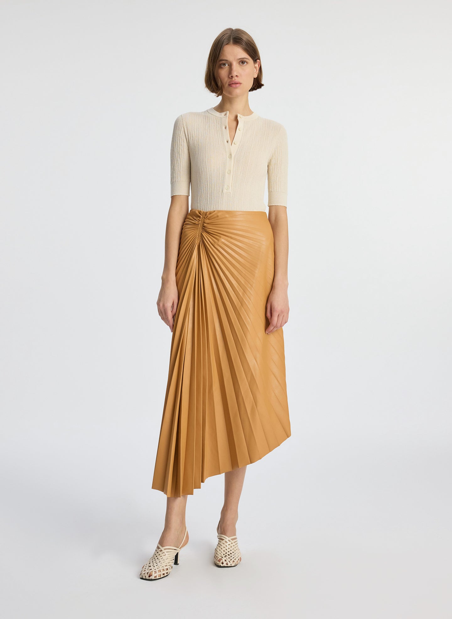 front view of a woman wearing beige shirt with brown pleated vegan leather midi skirt