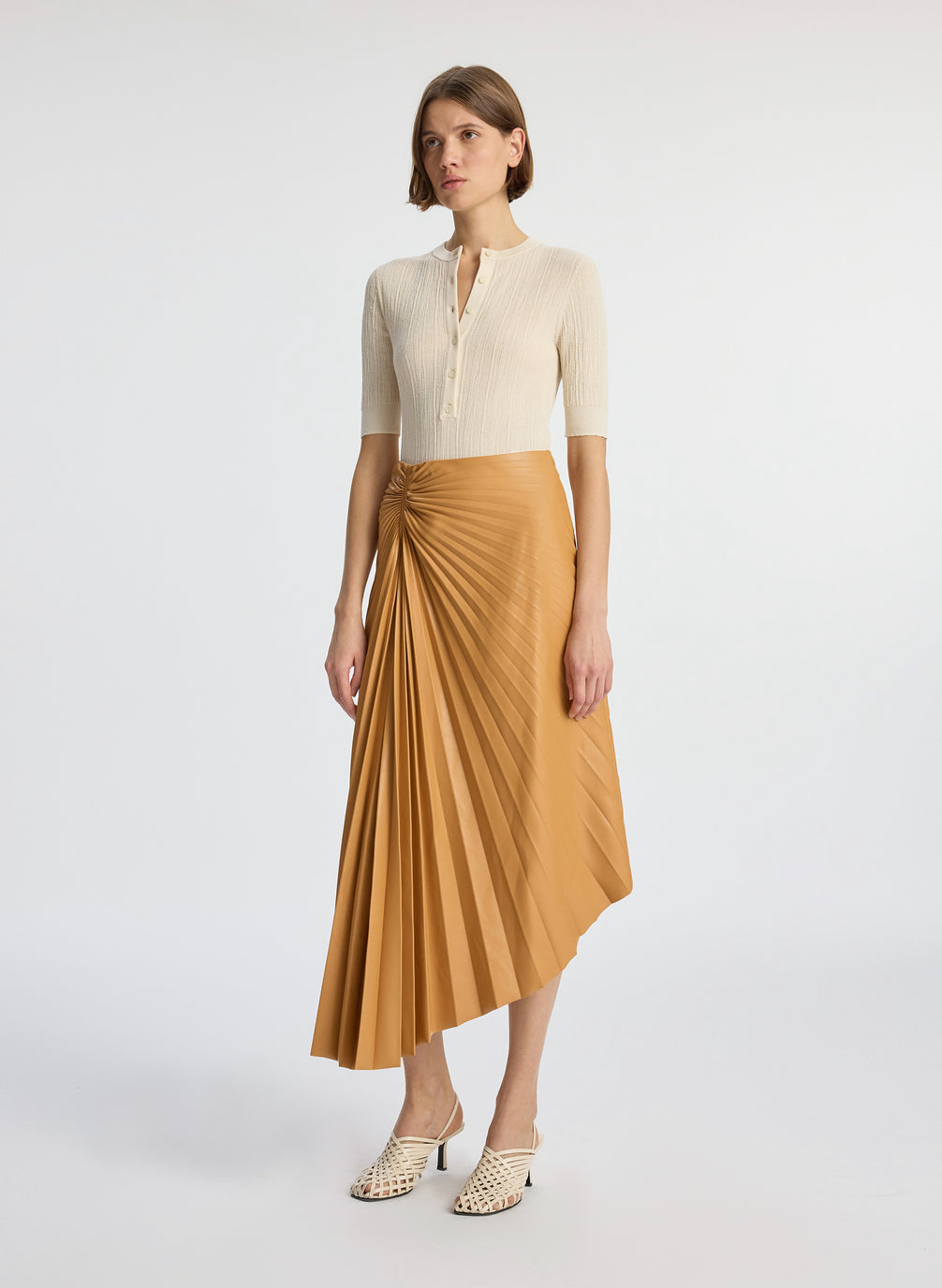 side view of a woman wearing beige shirt with brown pleated vegan leather midi skirt