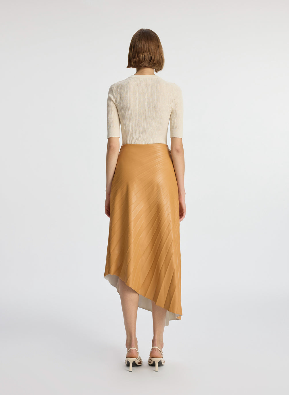 back view of a woman wearing beige shirt with brown pleated vegan leather midi skirt