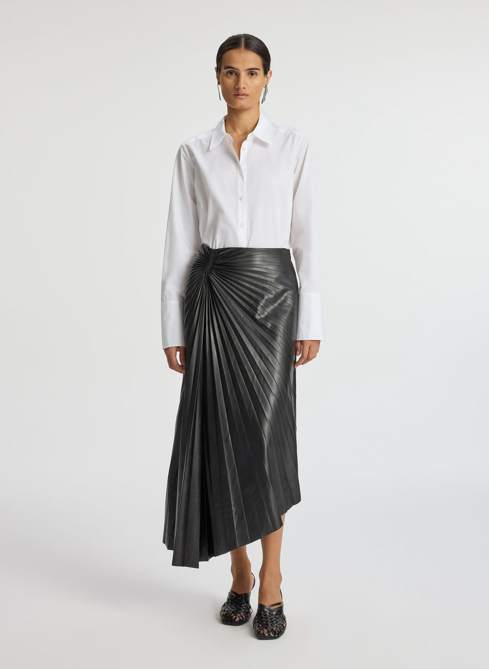 front view of woman wearing white button down top and black pleated vegan leather skirt