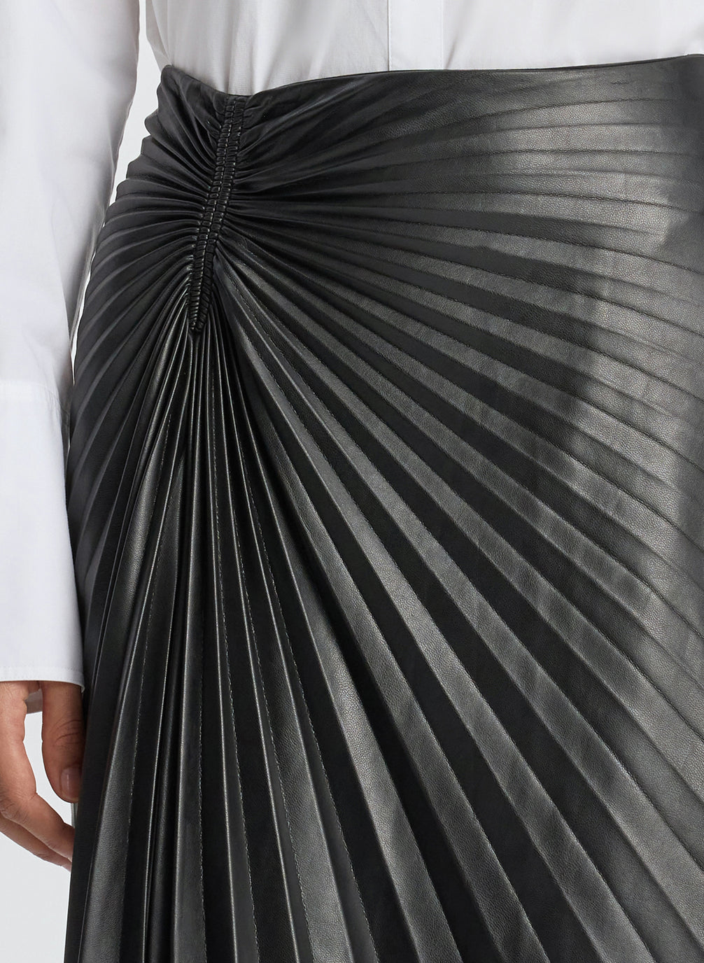 detail view of woman wearing white button down top and black pleated vegan leather skirt