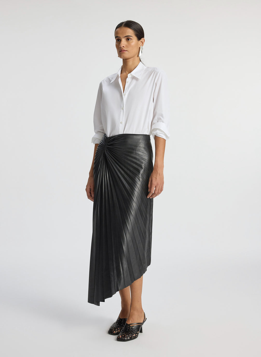 side view of woman wearing white button down top and black pleated vegan leather skirt