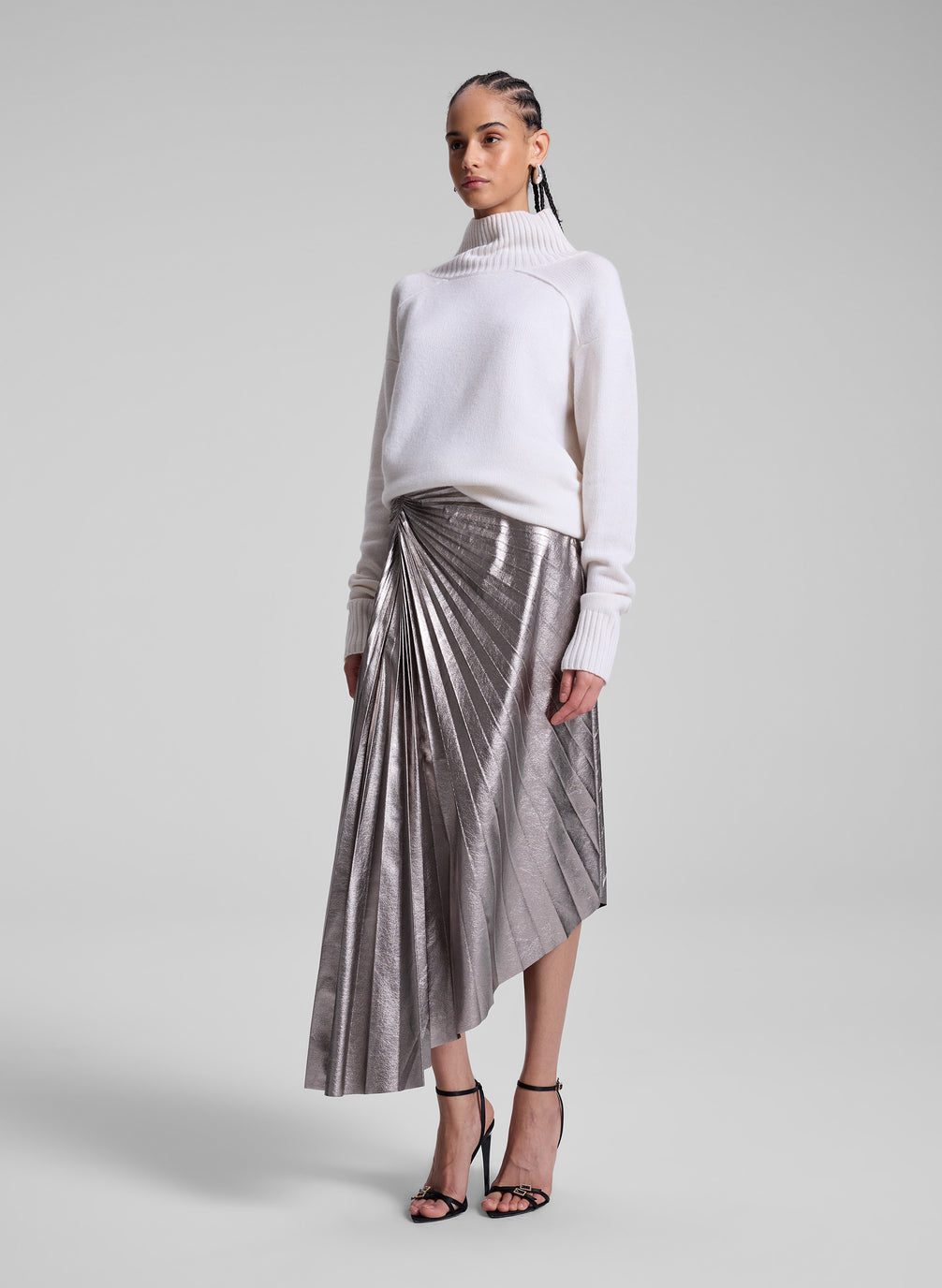 woman wearing white turtleneck sweater and grey metallic pleated skirt