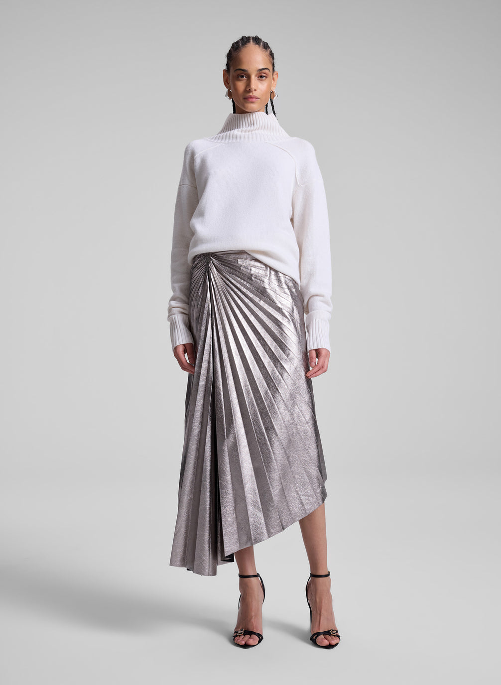 woman wearing white turtleneck sweater and grey metallic pleated skirt