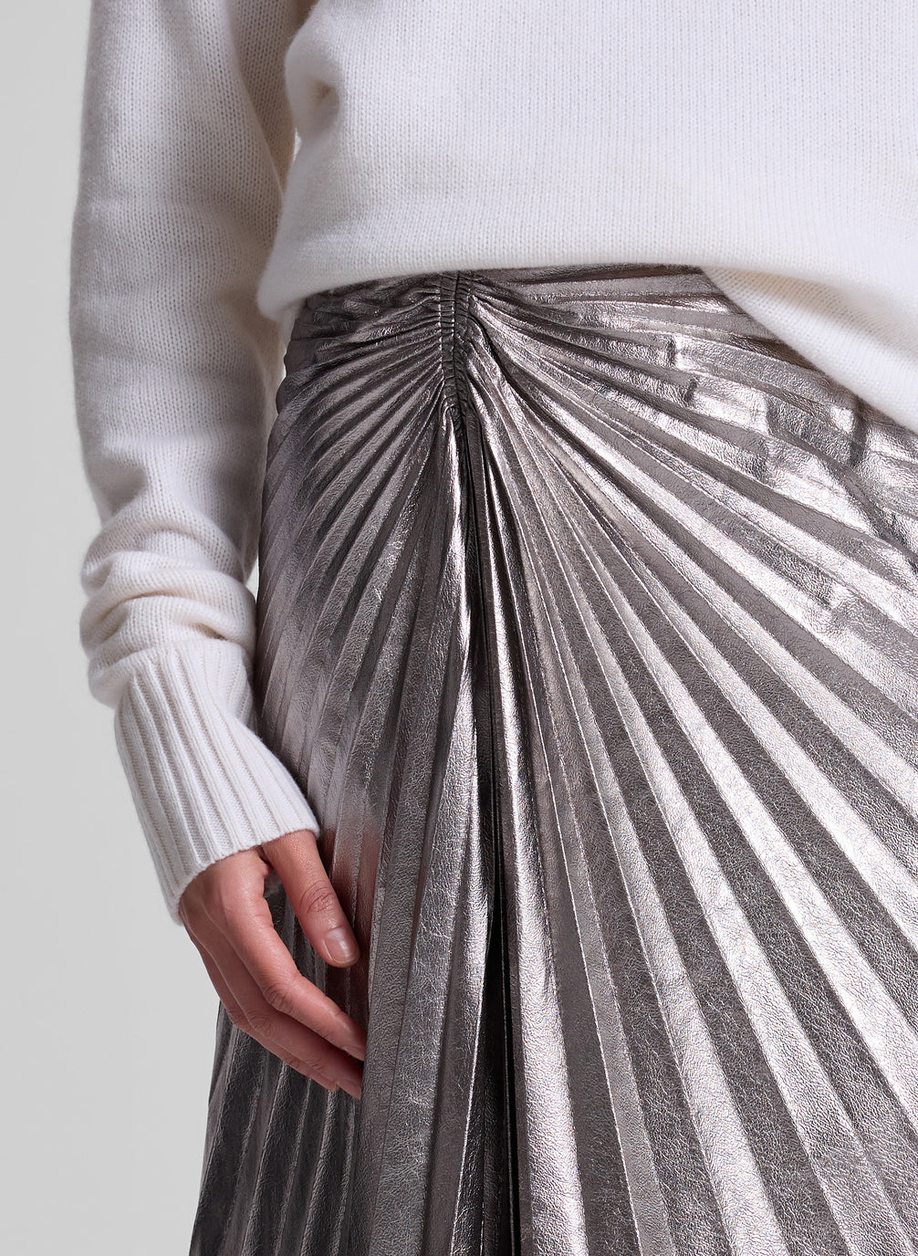 woman wearing white turtleneck sweater and grey metallic pleated skirt