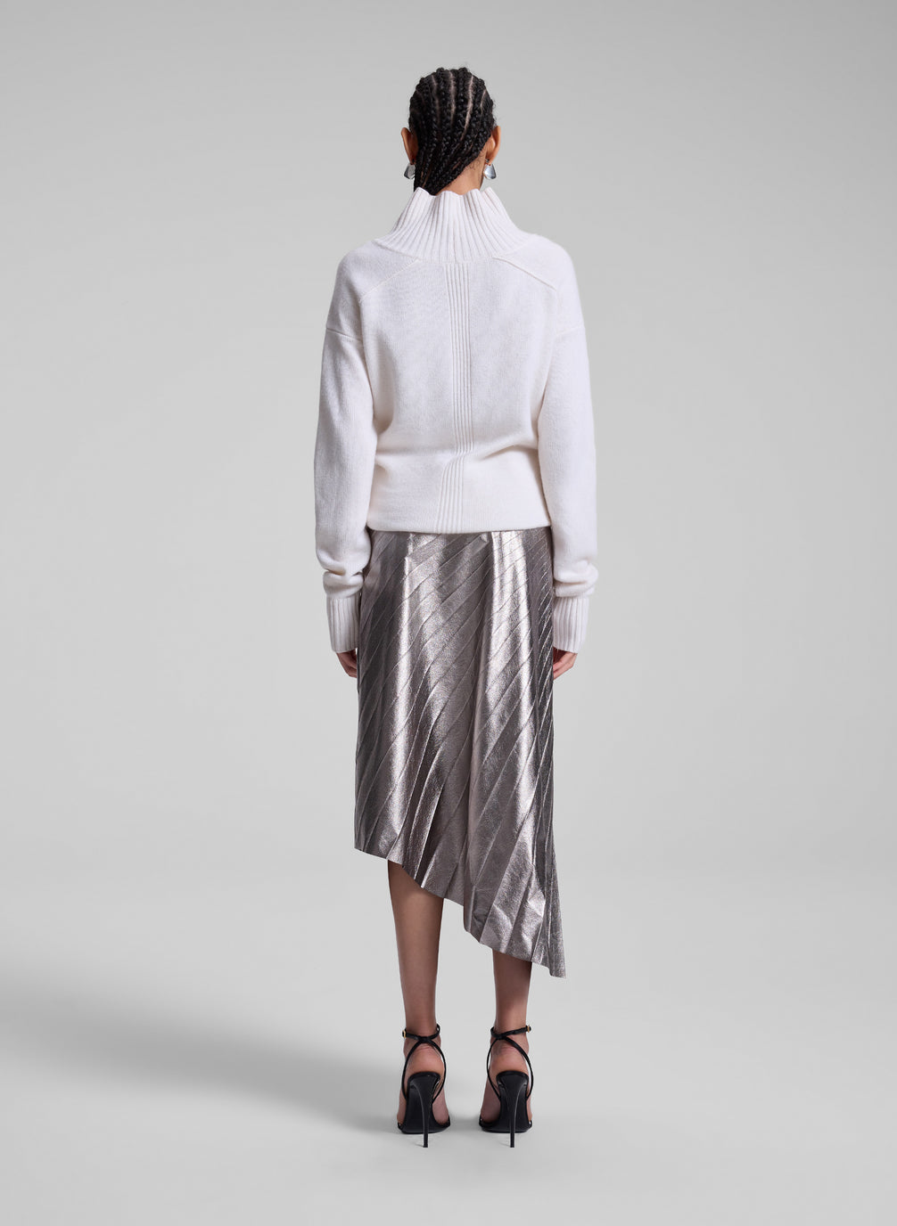 woman wearing white turtleneck sweater and grey metallic pleated skirt