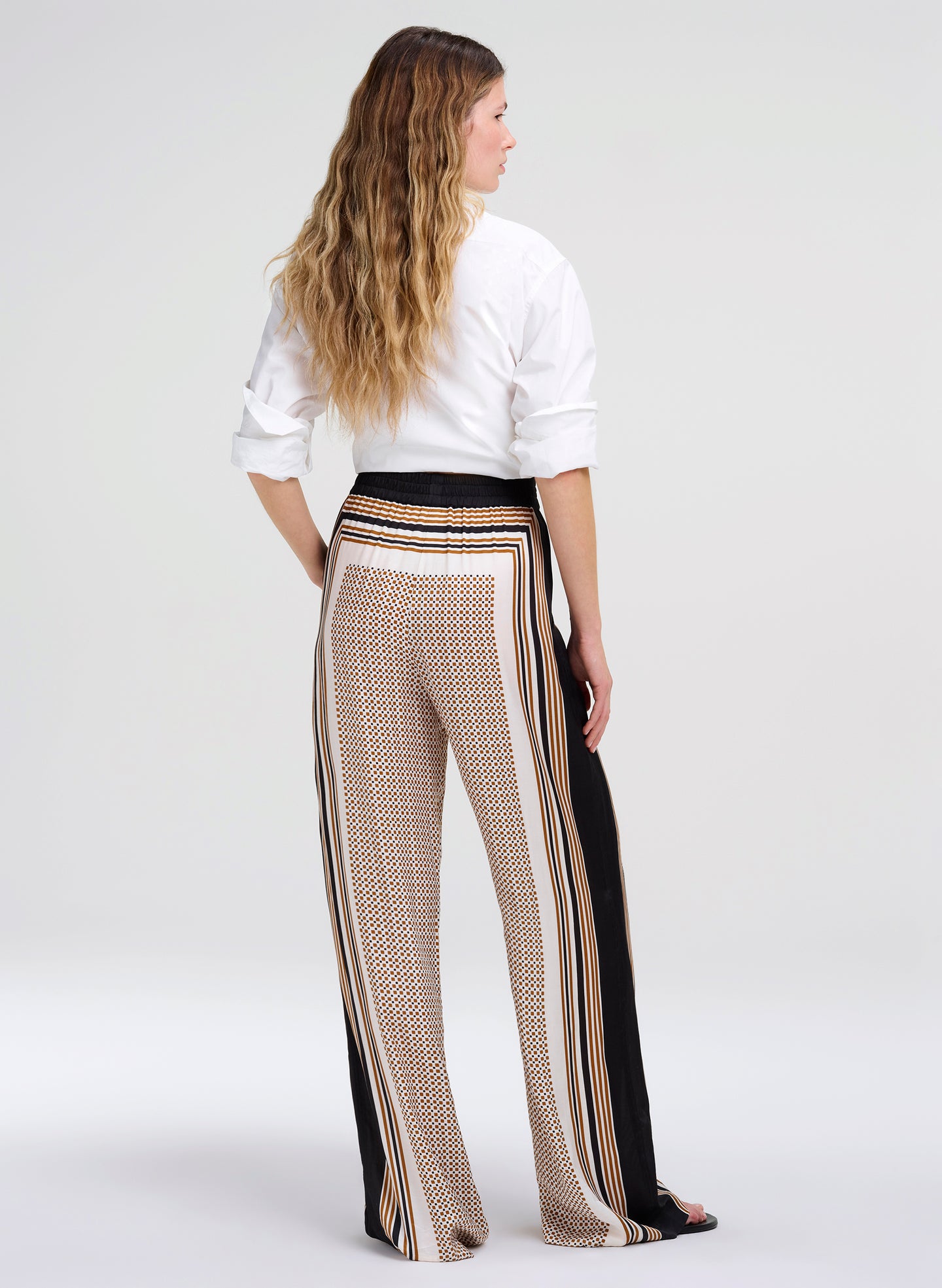 Woman wearing a white blouse and patterned pants on a white background