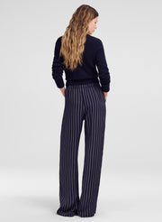 A woman shown from the back wearing a dark navy long-sleeve top and matching navy wide-leg trousers with thin white vertical pinstripes, photographed against a light gray studio background.
