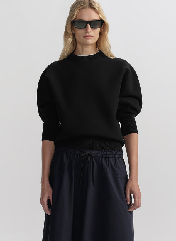 Person wearing a black sweater and blue skirt on a light gray background