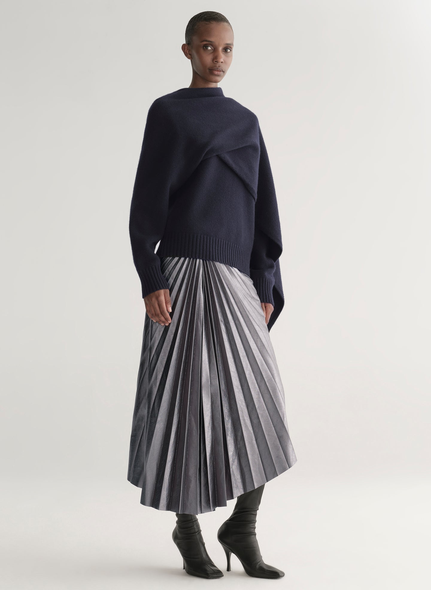 Person wearing a navy sweater and pleated skirt on a white background