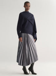 Person wearing a navy sweater and pleated skirt on a white background