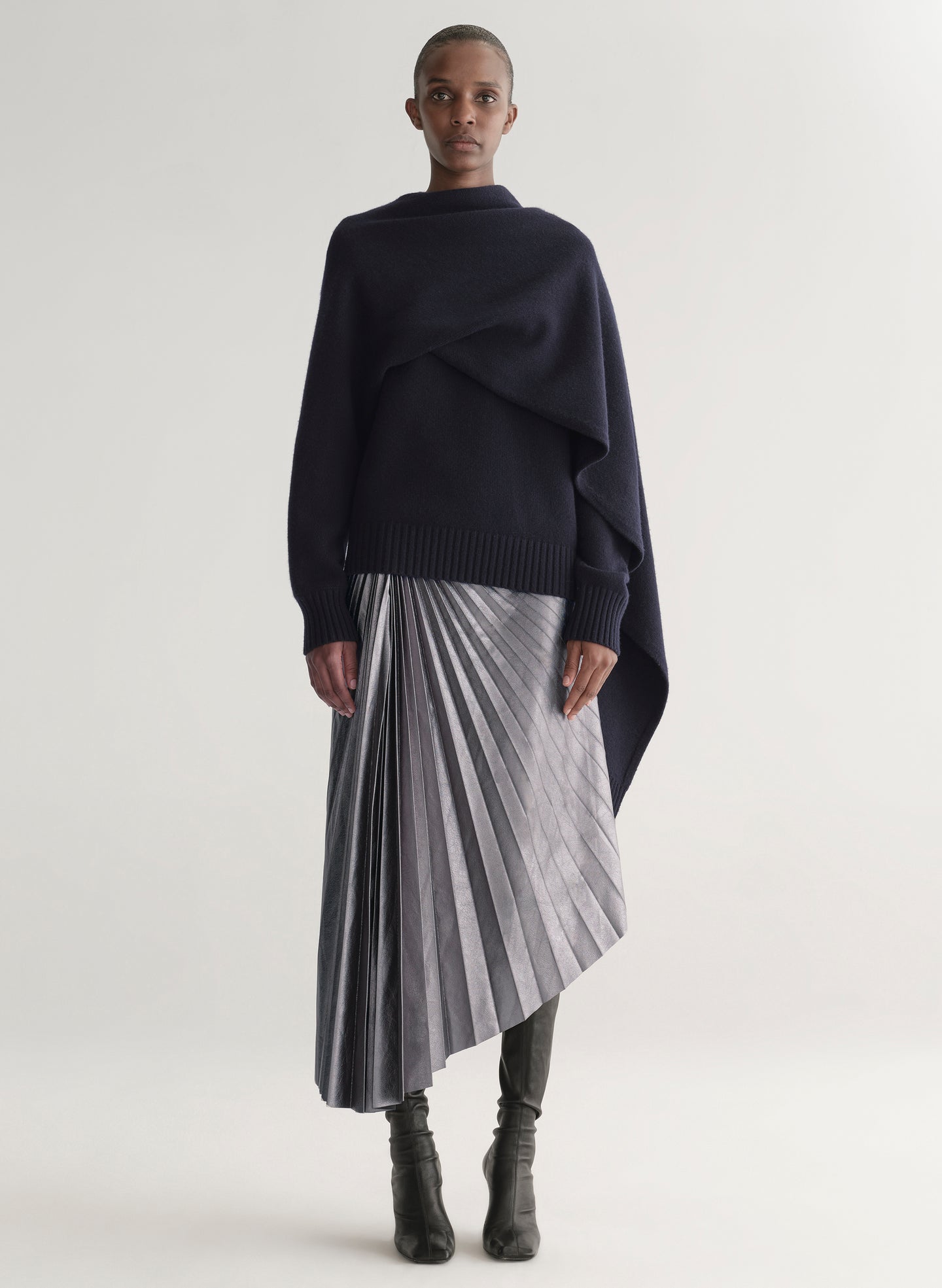 Person wearing a navy sweater and pleated skirt on a white background