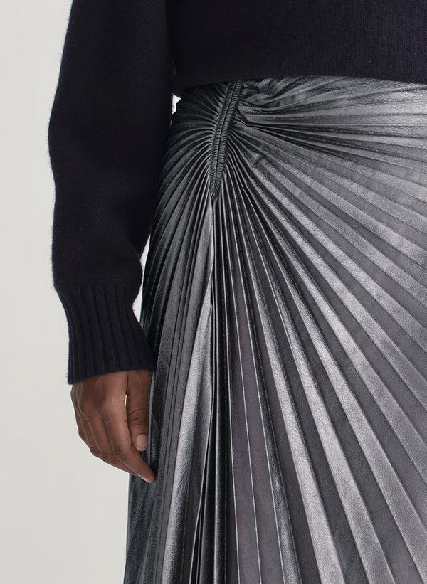 Person wearing a black sweater and pleated silver skirt on a light background