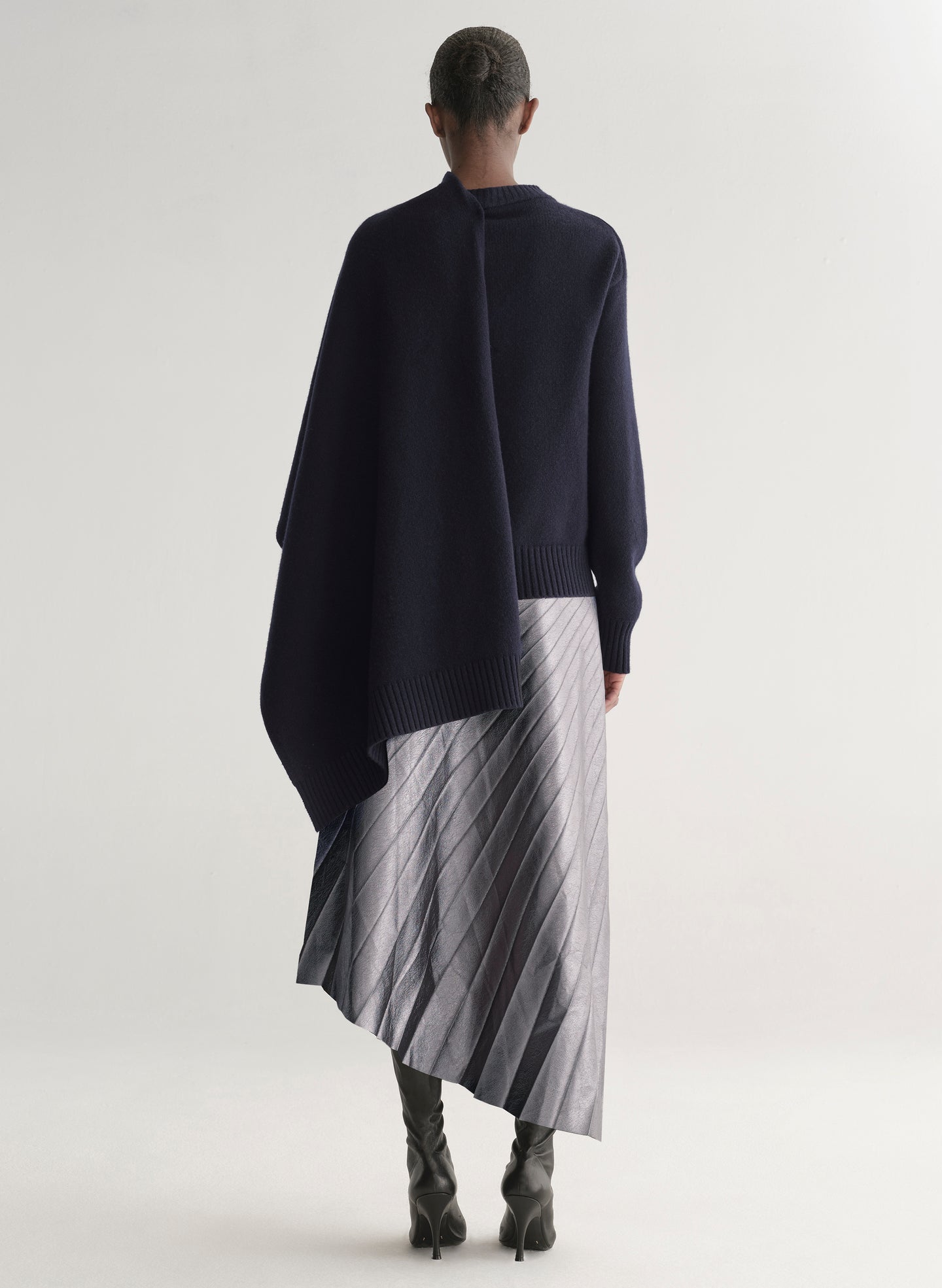 Person wearing a dark blue poncho over a striped dress on a white background