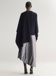 Person wearing a dark blue poncho over a striped dress on a white background