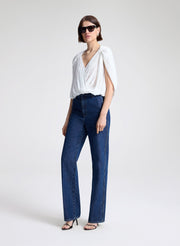 Woman wearing a white top and blue jeans with sunglasses on a light gray background