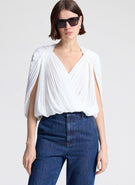 Woman wearing a white top and blue jeans with sunglasses on a light gray background