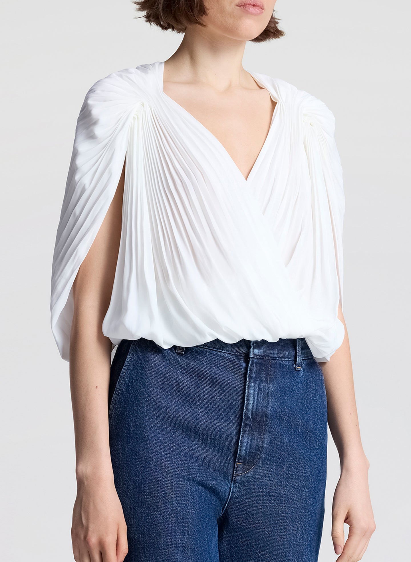 Woman wearing a white top and blue jeans with sunglasses on a light gray background