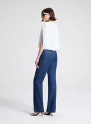 Woman wearing a white top and blue jeans with sunglasses on a light gray background