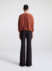 Person wearing a rust-colored blouse and black pants on a white background