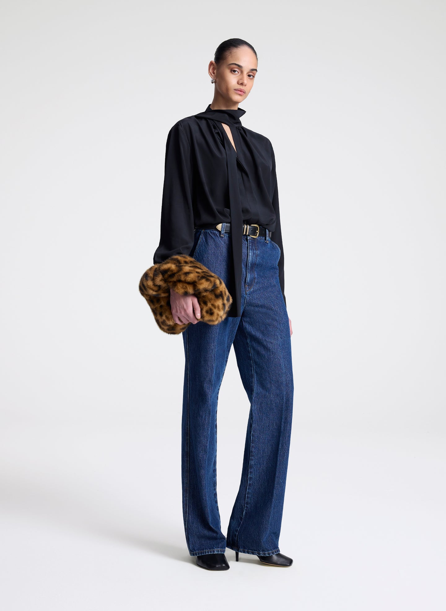 Woman wearing a black blouse and blue jeans holding a faux fur clutch against a white background
