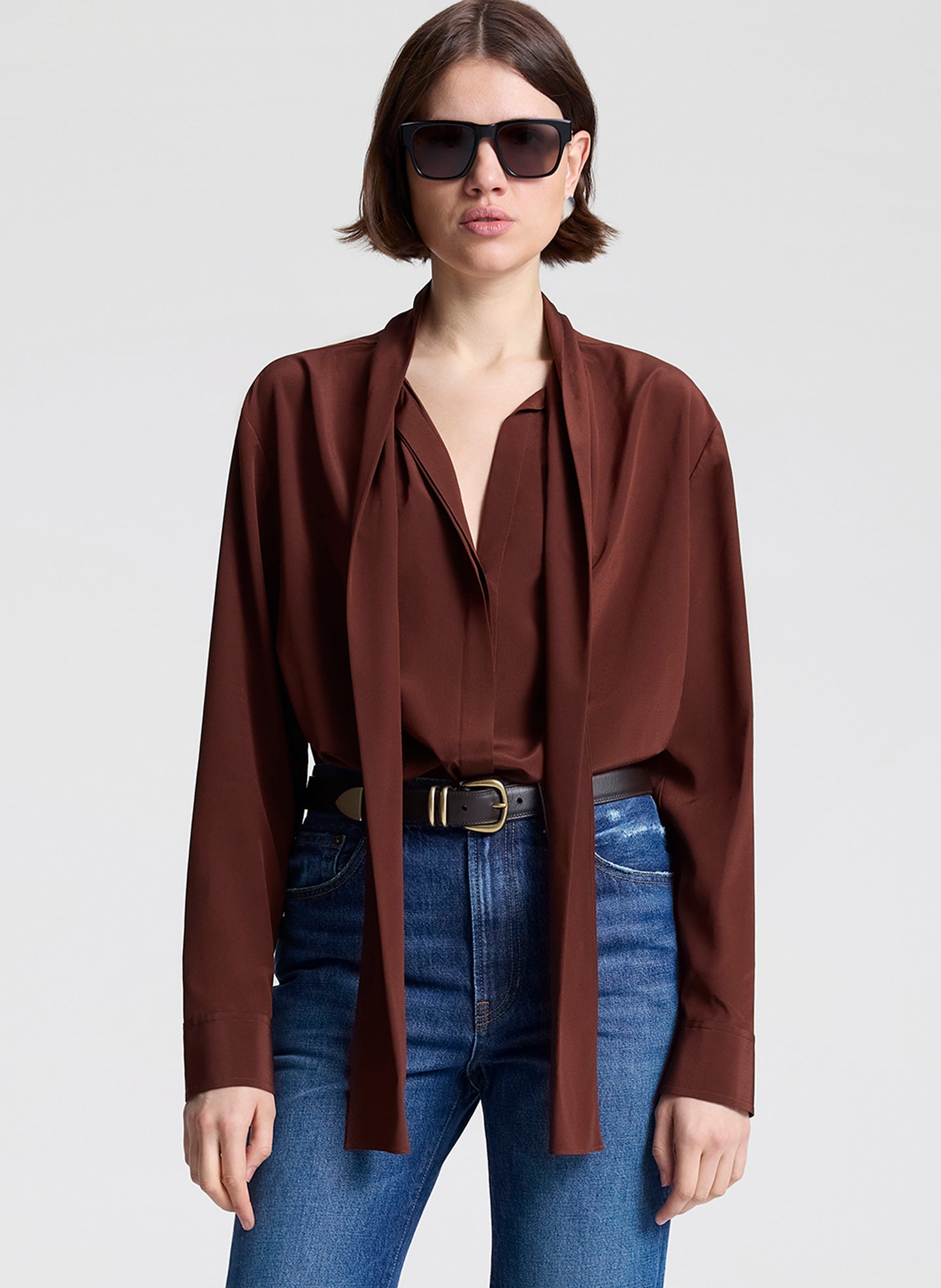 woman wearing burnt umber top, brown belt, and blue jeans