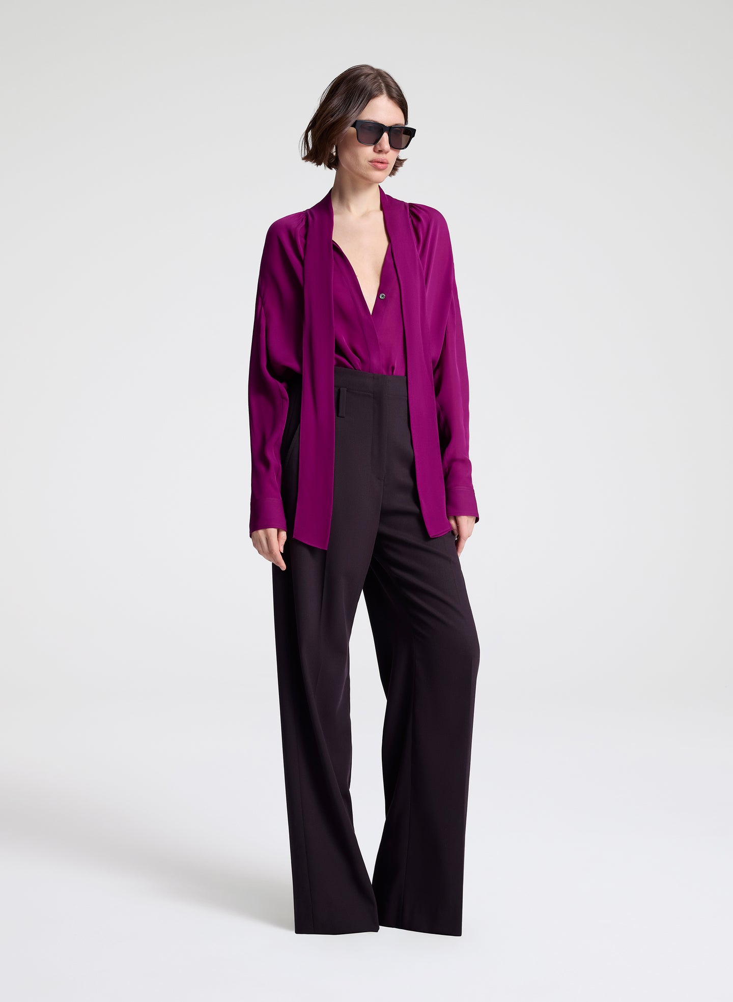 Woman wearing a purple blouse and dark purple pants on a white background