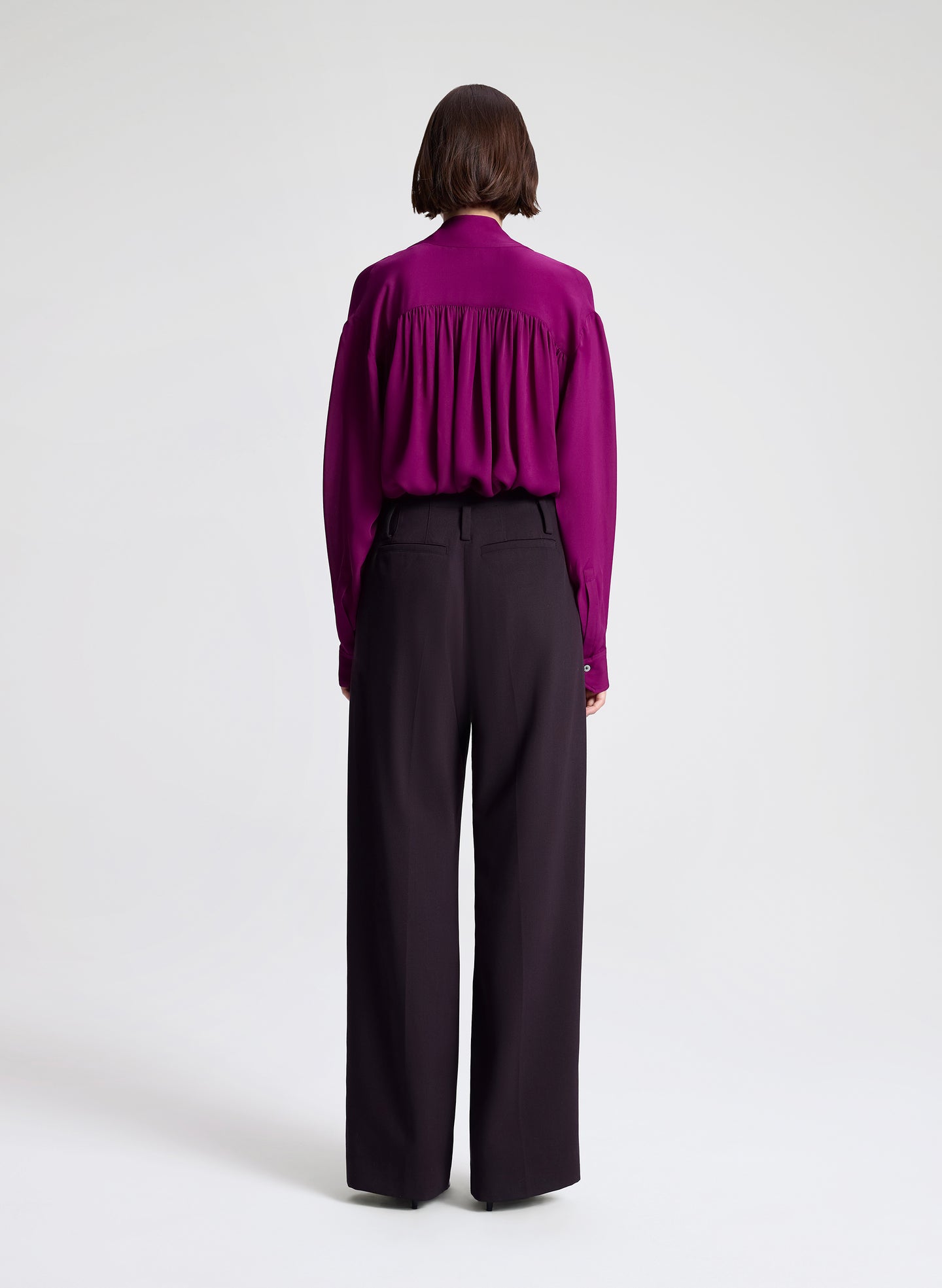 Woman wearing a purple blouse and dark purple pants on a white background