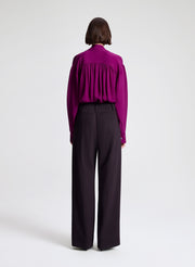 Woman wearing a purple blouse and dark purple pants on a white background