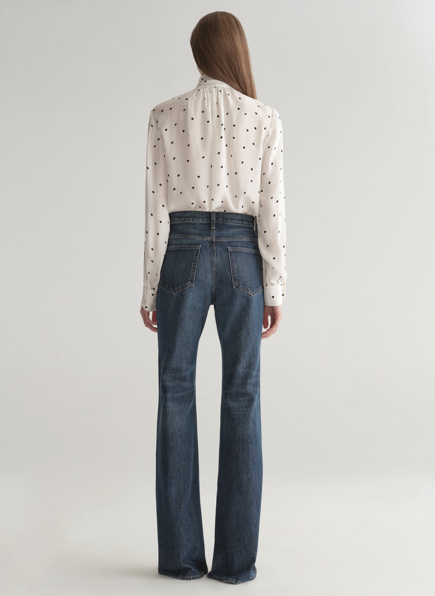 Woman wearing a polka dot blouse and jeans on a plain background