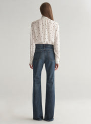 Woman wearing a polka dot blouse and jeans on a plain background