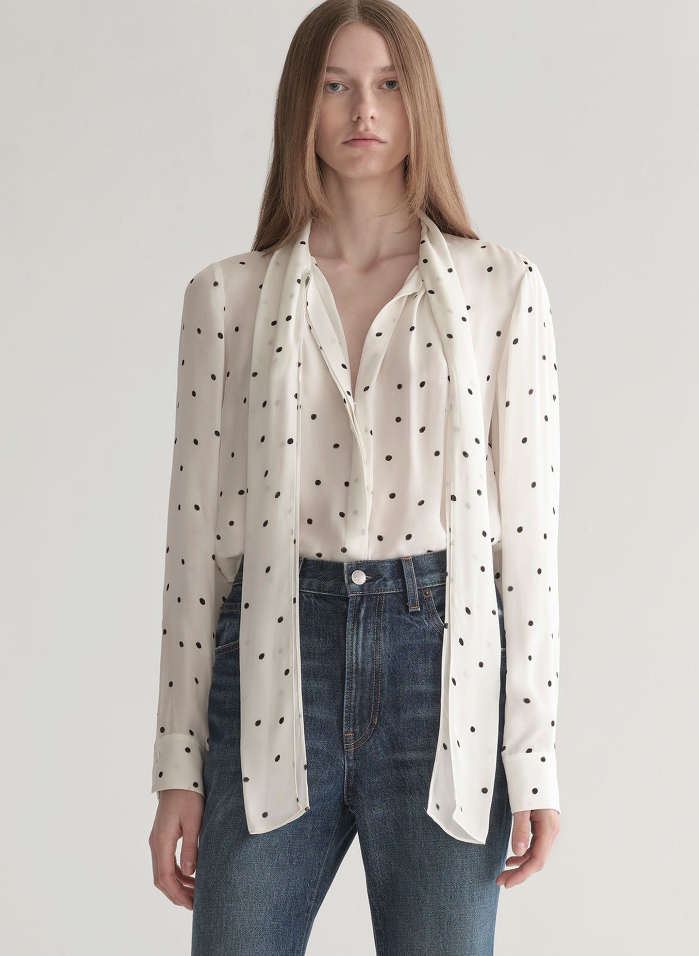Woman wearing a polka dot blouse and jeans on a plain background