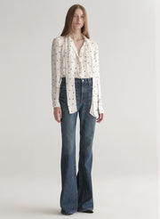 Woman wearing a polka dot blouse and jeans on a plain background