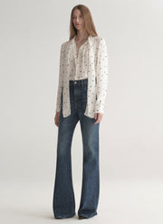 Woman wearing a polka dot blouse and jeans on a plain background