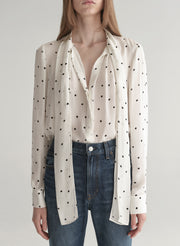 Woman wearing a polka dot blouse and jeans on a plain background