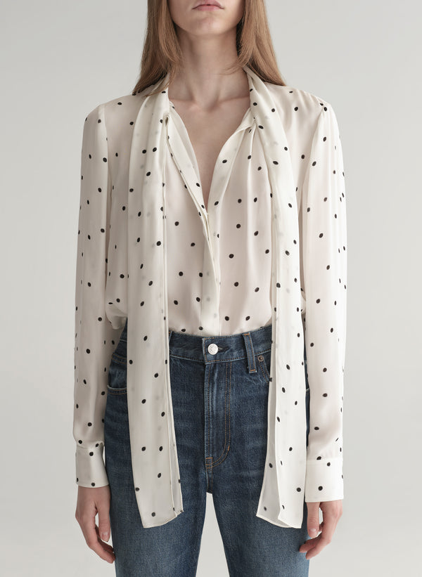Woman wearing a polka dot blouse and jeans on a plain background