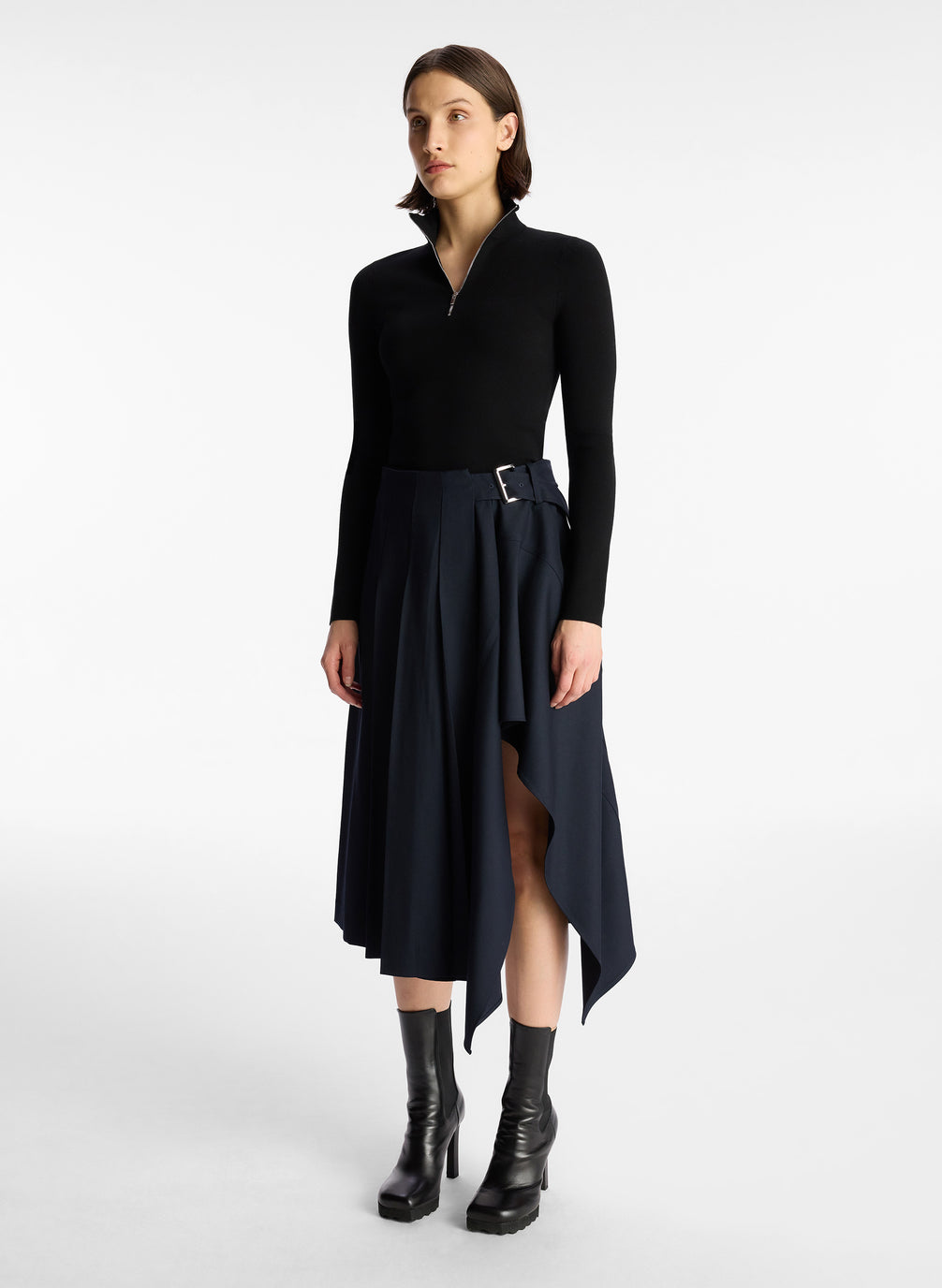 side view of woman in black long sleeve knit top and navy blue pleated skirt