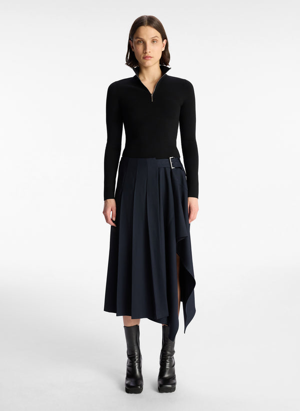 front view of woman in black long sleeve knit top and navy blue pleated skirt