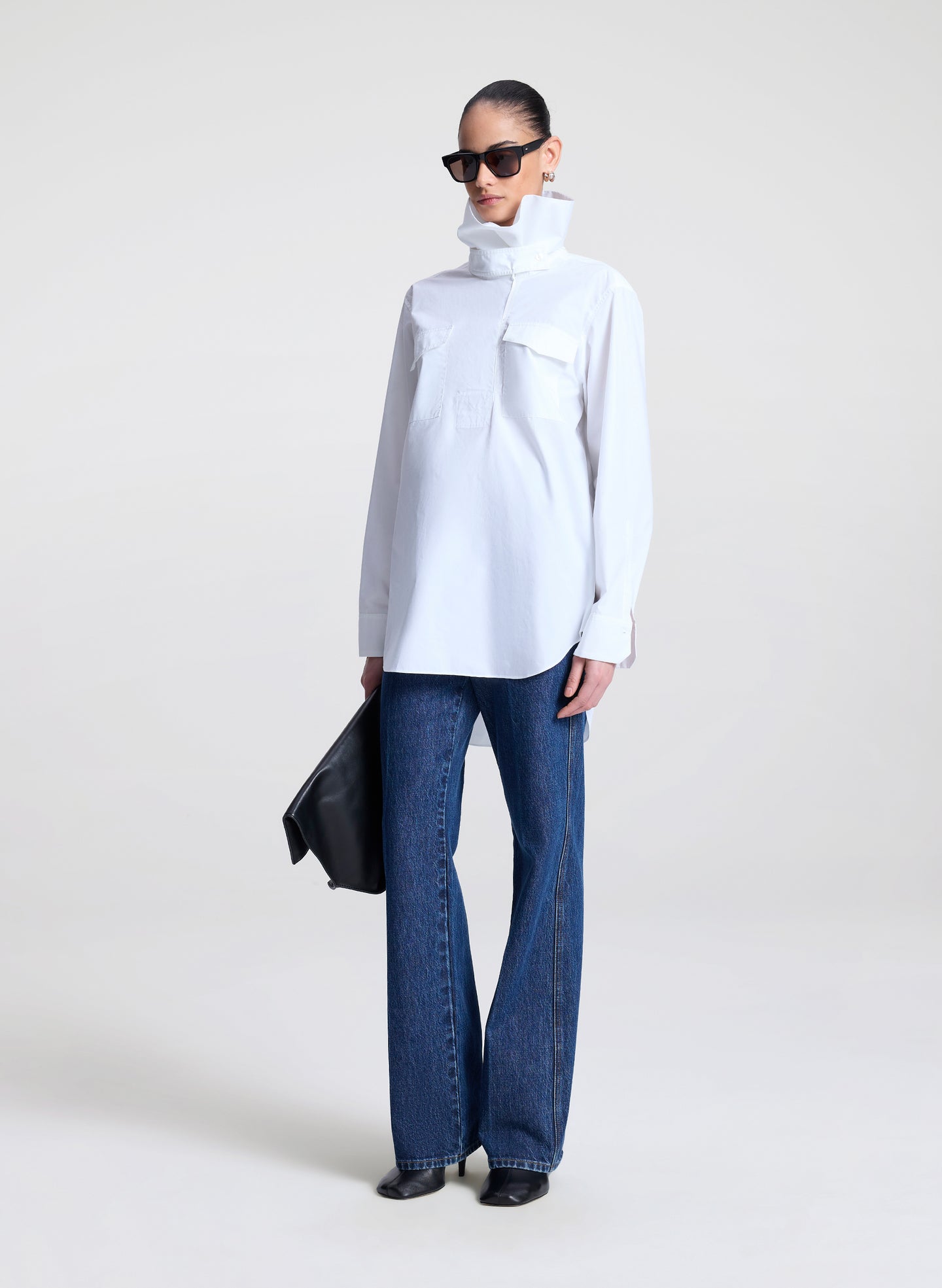 Person wearing a white collared shirt and blue jeans on a plain background