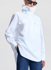 Person wearing a white high-neck shirt and blue jeans against a plain background