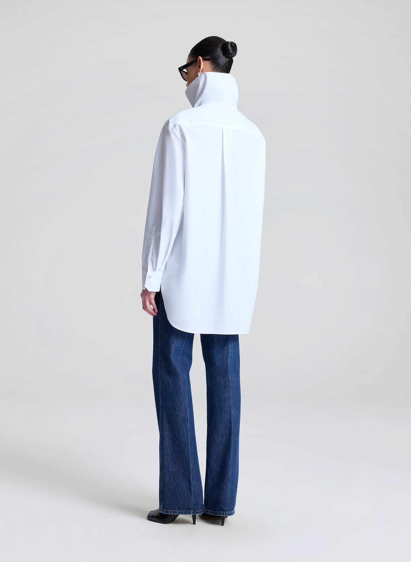 Person wearing a white collared shirt and blue jeans on a plain background